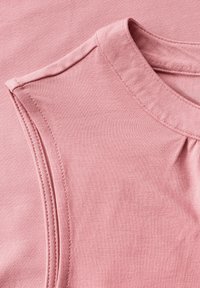 Débardeur rose clair sans manches avec un col rond, fabriqué en tissu doux. Présente des détails de couture subtils et un accent froncé à l'épaule.