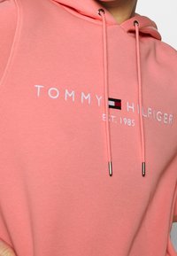 Sweat à capuche rose en mélange de coton, arborant un logo avec "TOMMY HILFIGER" et une date d'établissement. Comprend des cordons avec des embouts en métal.