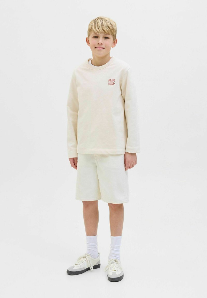 Sudadera de manga larga en color beige claro con logo bordado, combinada con pantalones cortos beige claro y zapatillas blancas. Ajuste simple y casual.