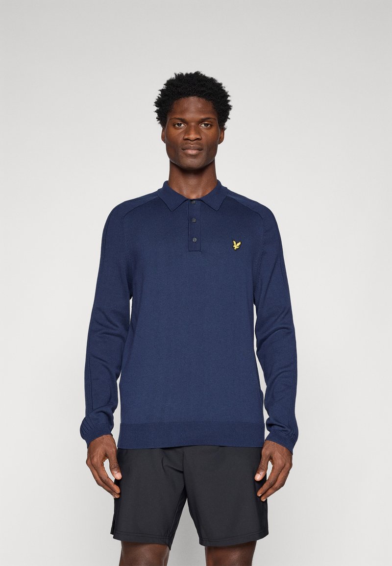 Jūras spēku garo piedurkņu polo krekls teksturētā dzijas audumā. Tam ir apkakle, trīs pogu slēgšana un mazs dzeltenais logotips uz krūškurvja.