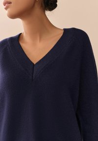 Marineblauer, gestrickter Pullover mit V-Ausschnitt, weicher Textur und dezenten Rippdetails am Kragen und den Schultern.