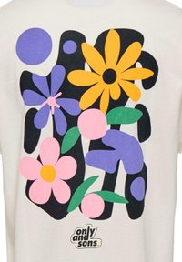 T-shirt crème avec des motifs floraux colorés en violet, rose, jaune et noir, avec un petit logo en bas.