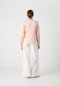 Blusa rosa chiaro con maniche lunghe e scollatura rotonda, abbinata a pantaloni bianchi a gamba larga. Texture liscia, design minimale.