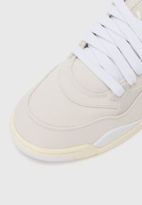 Beige színű sneaker fehér fűzőkkel, texturált vászon felső részel, párnázott bokarésszel és rugalmas, enyhén ívelt formájú gumitalppal.