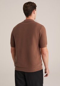 Hnědá pletená polo tričko s krátkým rukávem, strukturovaná tkanina, žebrovaný límec a lem, v kombinaci s černými kalhotami. Pohled zezadu.