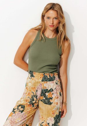 Débardeur côtelé vert olive avec encolure ronde, associé à un pantalon large à motifs floraux dans des tons orange, rose et vert.