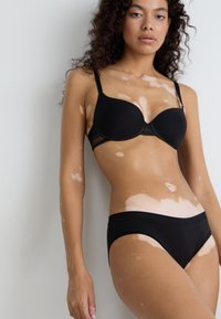 Black padded bra and matching low-rise panties in smooth fabric, featuring adjustable straps and a seamless design. Skin tone variations visible.