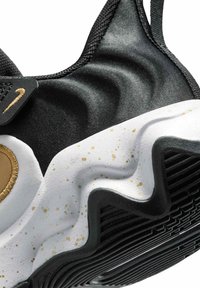 Zapatilla negra con parte superior texturizada, acentos dorados y una suela blanca ondulada con manchas doradas y suela de goma negra.