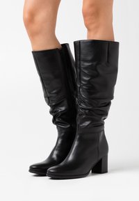Black leather knee-high boots with a rounded toe, textured body, zipper detail on the side, and a chunky, block heel.