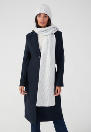 Marineblauer Mantel mit zwei Knöpfen, kombiniert mit einem hellgrauen gerippten Schal und passender Strickmütze. Weiche Texturen, elegantes Design und gemütliches Erscheinungsbild.