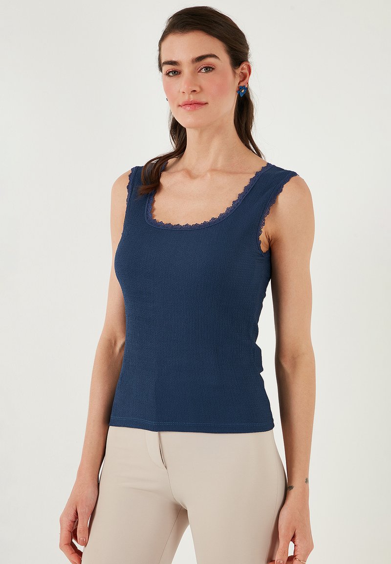 Top da mare in navy con scollatura a girocollo, spalline sottili e bordo in pizzo. Realizzato in tessuto testurizzato, silhouette aderente e si allunga dolcemente.