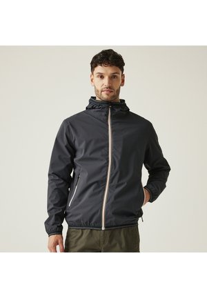 Man wearing a black zip-up hooded jacket with a front zipper and zippered pockets, standing against a plain light background.