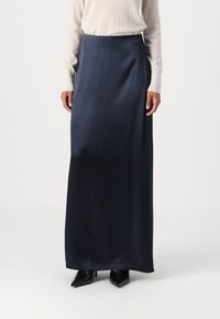 Navy zijden maxirok met een gladde textuur, voorzien van een rechte snit en subtiele glans. Gecombineerd met een beige langemouwen top en zwarte schoenen.