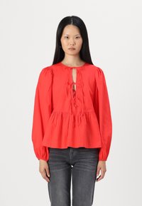 Blusa di cotone rossa con scollatura rotonda, dettaglio a chiave, maniche lunghe a palloncino e vita peplo arricciata.