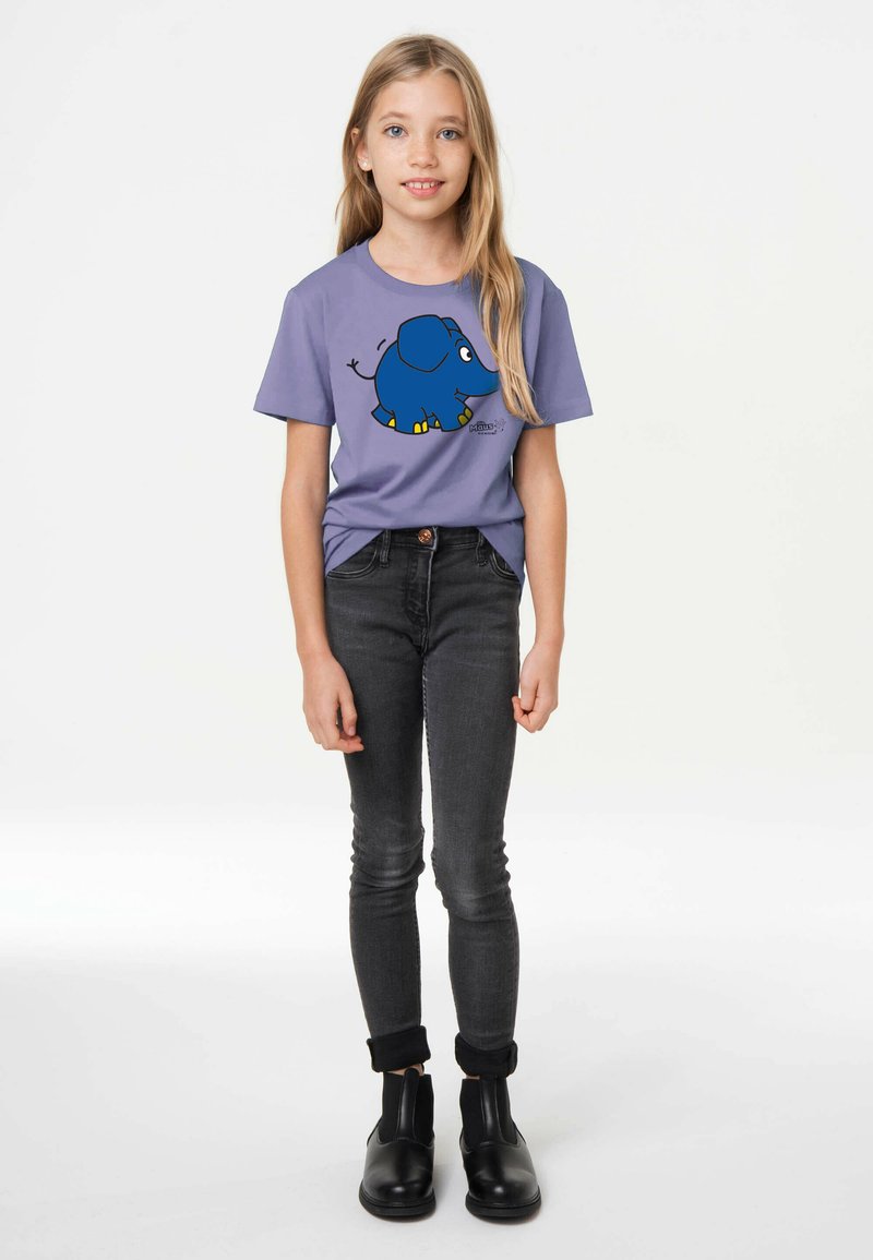 Lila T-Shirt mit einem blauen Cartoon-Elefantendesign, kombiniert mit eng anliegenden grauen Jeans und schwarzen Stiefeletten mit elastischen Einsätzen.
