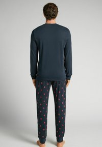 Top de manga larga azul oscuro combinado con pantalones de pijama a juego que presentan un patrón repetido en rojo con pequeños diseños. Tela suave con puños acanalados.