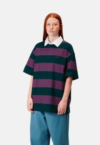 Camisa polo a rayas en verde y morado, con un color blanco y mangas cortas. Combinada con pantalones sueltos en color azul verdoso.