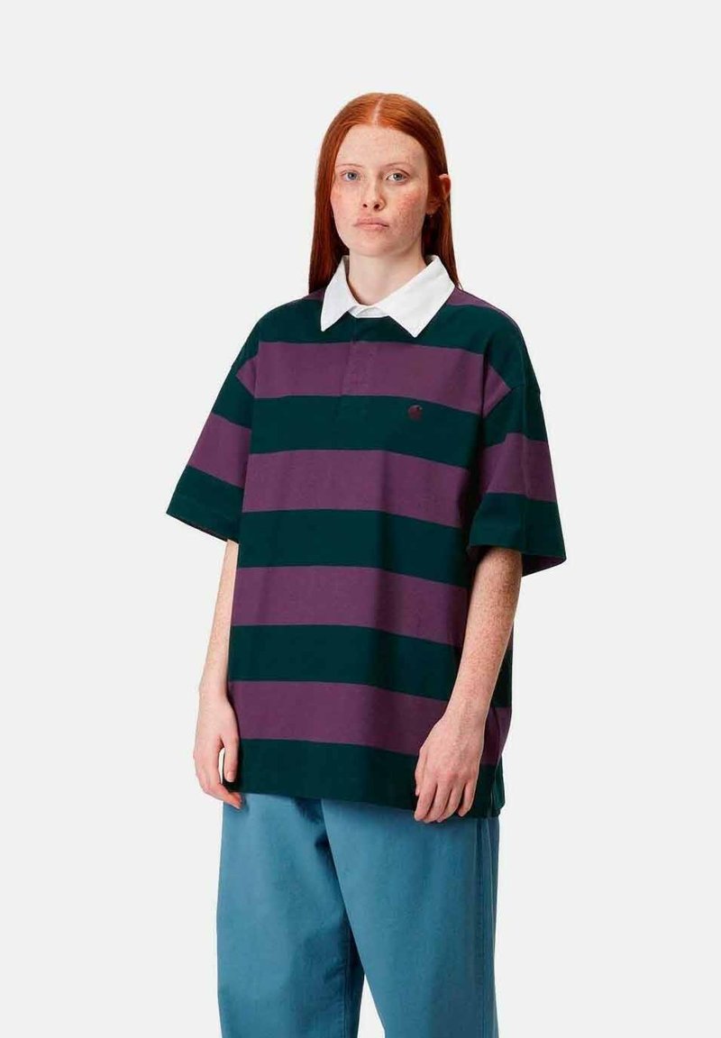 Camisa polo a rayas en verde y morado, con un color blanco y mangas cortas. Combinada con pantalones sueltos en color azul verdoso.