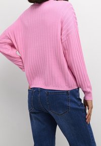 Pull côtelé rose à manches longues, avec un col rond plongeant et une coupe décontractée, associé à un jean en denim bleu foncé.