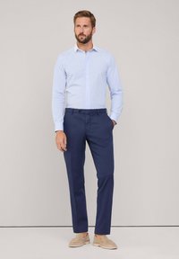 Camisa de manga larga a rayas en azul claro y blanco, combinada con pantalones marinos y calzado de lona beige. Diseño sencillo con detalles de botones.