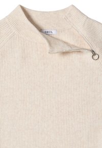 Sweter w kolorze kremowym z prążkowaną teksturą, z kołnierzykiem na zamek i małym kółkiem jako uchwytem. Widoczna etykieta z napisem "CECIL".