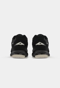 Black athletic shoes with a textured mesh upper, padded collar, and reflective detailing. The sole features black and gray cushioning elements.