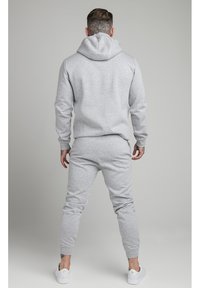 Conjunto de sudadera gris con capucha y pantalones de chándal, hecho de un tejido suave, que presenta un diseño ajustado y puños acanalados, con un bolsillo tipo canguro y capucha con cordón.