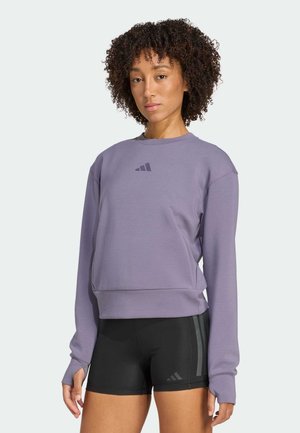 Felpa viola con scollo rotondo e maniche lunghe, caratterizzata da un piccolo logo nero sul petto, abbinata a pantaloni sportivi neri con strisce.