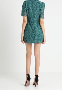 Tyrkysové krajkové šaty s květinovým vzorem, krátkými rukávy a zipem na zadní straně. V kombinaci s černými sandály na vysokém podpatku s kotníkovými řemínky.