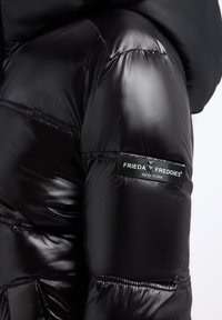 Czarna, błyszcząca kurtka puchowa z przeszyciami i naszywką z logo "Frieda & Freddies New York" na górnym ramieniu.