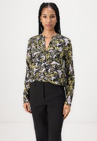 Blomstrete bluse med mønster i svart, gult og lavendel, med dyp V-hals, lange ermer og et mykt stoff, kombinert med svarte bukser.