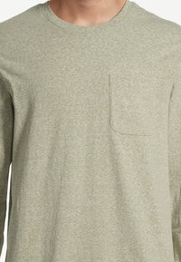Long-sleeve, light olive green T-shirt made from soft cotton blend. Features a pocket on the left chest and a round neckline.