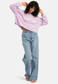 Purple cropped sweatshirt with white graphic text, paired with loose, light blue denim jeans featuring a high waist and classic five-pocket design.