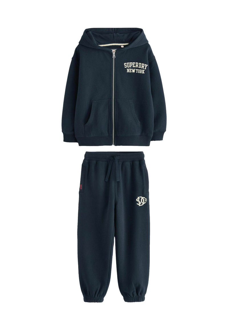 Sudadera azul marino con capucha, cierre frontal y bolsillos delanteros. Pantalones de chándal a juego en azul marino con cintura elástica y bordado del logo.