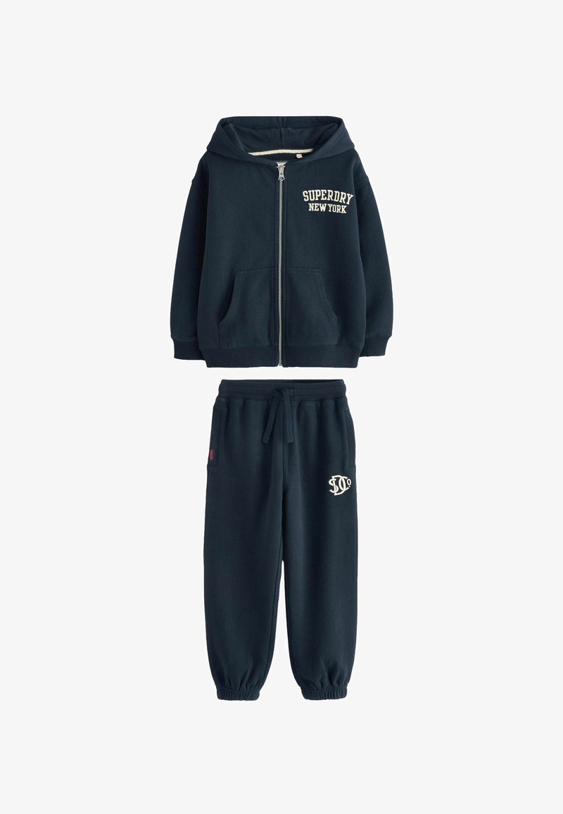 Granatowa bluza z kapturem, na zamek z przodu i kieszeniami z przodu. Pasujące granatowe dresy z elastycznym pasem i haftowanym logo.