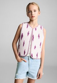 Quilted sleeveless vest in cream with purple abstract patterns, featuring a rounded neckline and pink trim, paired with denim shorts.