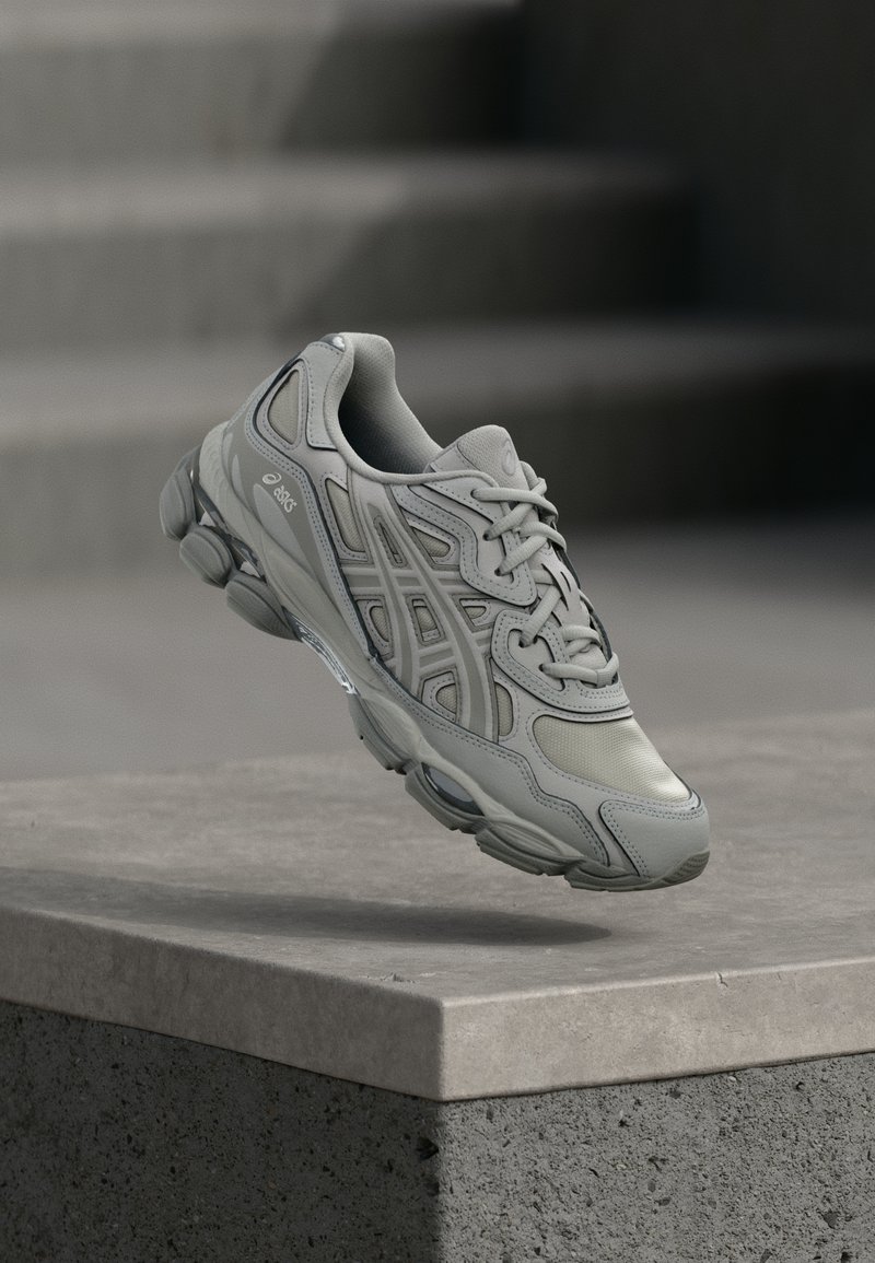 Svetlo sivi atletski čevlji s kombinacijo gladkih in teksturiranih površin, z zračno mrežico na zgornjem delu, zaobljenim nosom in oblazinjenim podplatom.