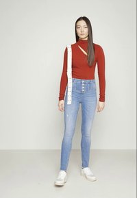 Top vermelho de gola alta com detalhe recortado, combinado com jeans de cintura alta azul clara com fecho de botão e detalhes em cinto branco.