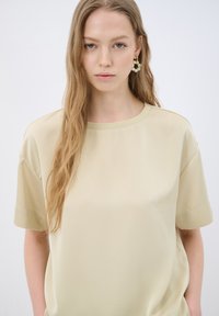 Lys beige kortærmet t-shirt lavet af glat stof med en afslappet pasform og en rund halsudskæring. Bemærkelsesværdig for sit minimalistiske design.