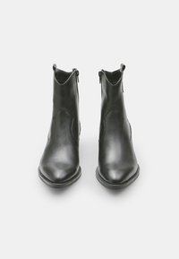 Botas de cuero negro hasta el tobillo con punta afilada, cierre con cremallera y textura suave. Presentan un diseño de corte angular en los lados.