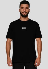 Černé bavlněné tričko s krátkým rukávem a kulatým výstřihem. Na hrudi je bílé text „WRONG FRIENDS“ umístěné na střed. Jednoduchý design.