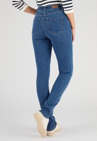 Jeans en denim bleu skinny avec poches arrière, taille haute et délicate patine. Complétés par des baskets blanches.