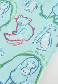 Světle modré bavlněné tričko se zvířecími ilustracemi: panda, tučňák a gorila, s barevnými textovými akcenty a grafickými vzory.