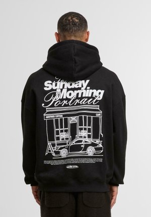 Black hoodie featuring a graphic print on the back of a café and a car in white, with a large text overlay. Made from cotton with a relaxed fit.