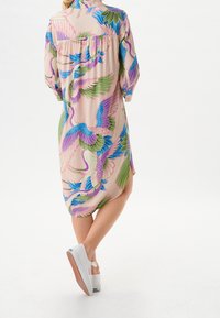 Abito a maniche corte in tessuto leggero con un motivo colorato di uccelli e foglie su uno sfondo rosa. Scarpe platform bianche con suola texturizzata.