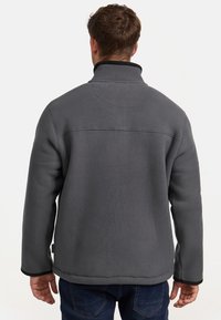 Chaqueta de forro polar gris con cuello alto, con ribetes negros y una textura suave. Una línea de costura atraviesa la parte superior de la espalda.