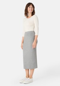 Lehký krémový top s dlouhým rukávem v kombinaci se středně dlouhou šedou úpletovou sukní. Má přiléhavý střih a pohodlné bílé tenisky.