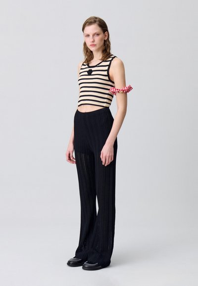 Pantalons en tricot noirs avec des côtes verticales associés à un haut cropped noir et beige à rayures, doté d'un col rond et d'une bordure en dentelle. Accent sur les bras à carreaux rouges.