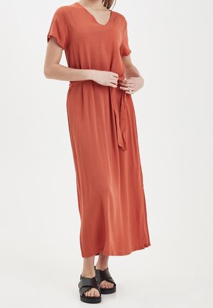 Rostfärgad maxiklänning med korta ärmar, V-ringning, en fastsydd knytbälte och en löst fallande passform. Kombinerad med svarta sandaler.