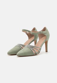 Escarpins en suède vert avec un bout pointu, une bride de cheville et des bandes décoratives en cristal à l'avant. Design à talon aiguille.